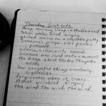 Black and white photo of notebook with a gratitude poem, a canon lengs, and coffee cup.